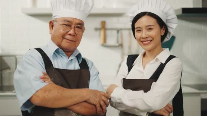 两个快乐的厨师在他的厨房里交叉站着的肖像。