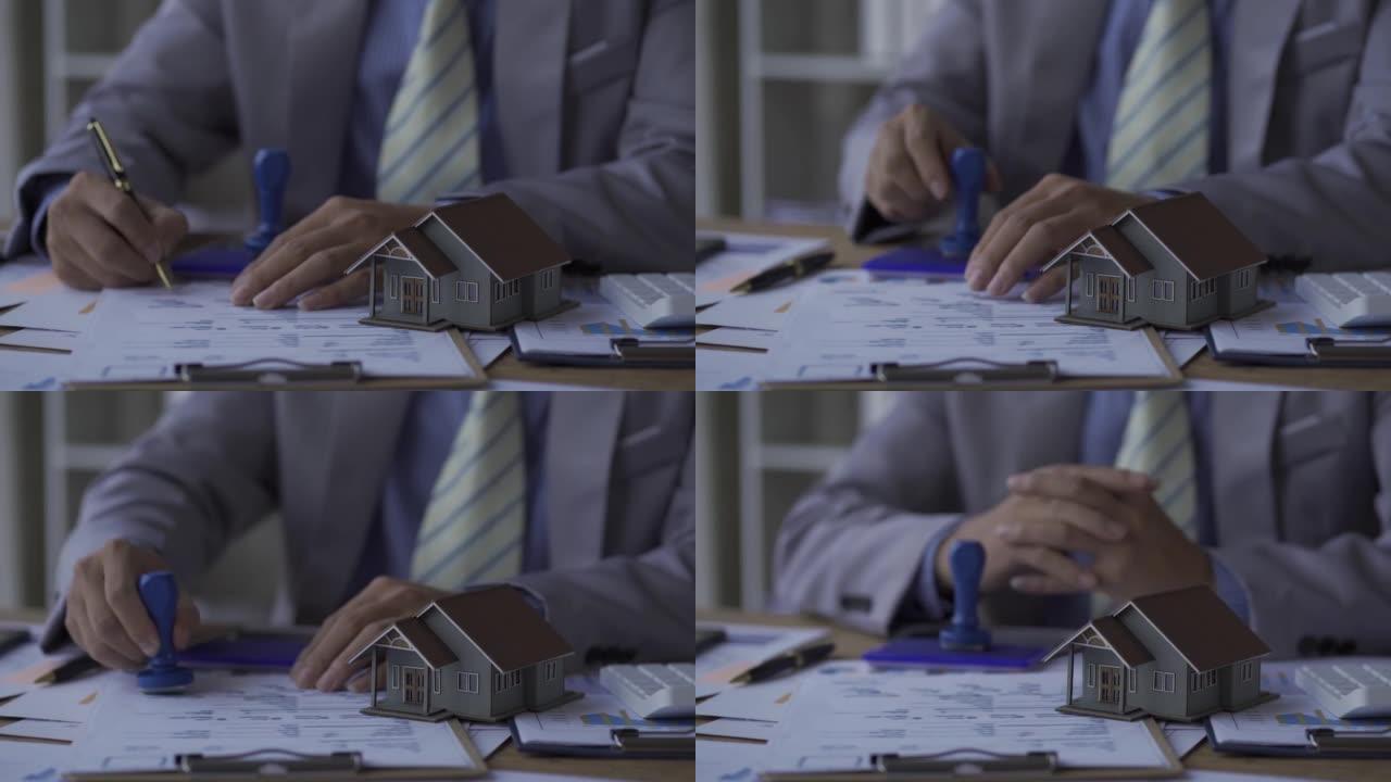 一位商人签订了购买新房的合同。房地产经纪人办公室桌子上的微型模型房屋。合同是在房子的建筑模型后面签的