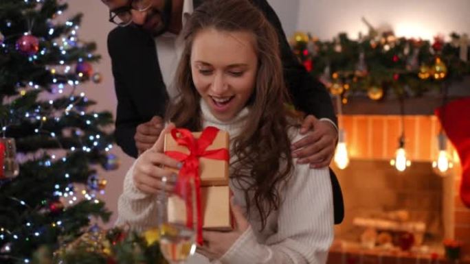 兴奋的高加索女友的肖像在慢动作中打开中东男友的圣诞礼物感谢伴侣。快乐的爱心女人在假期收到男人的新年礼