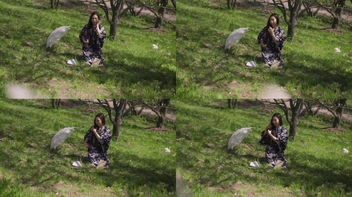 亚洲苗条的年轻美女坐在阳光明媚的公园绿色的春天草地上抚摸头发。自信优雅的日本千禧一代在户外阳光下休息