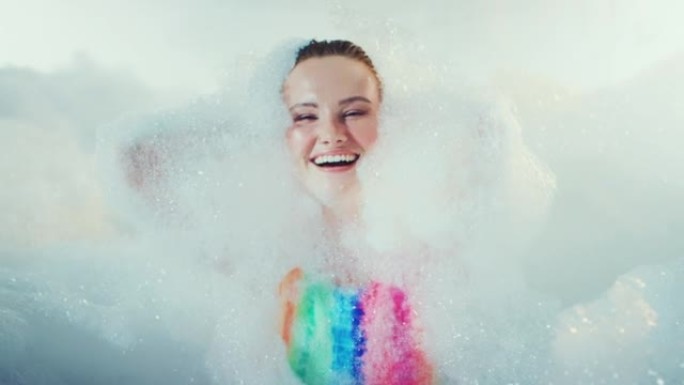 快乐美丽的女人快乐而轻松地覆盖着沐浴泡沫。慢动作