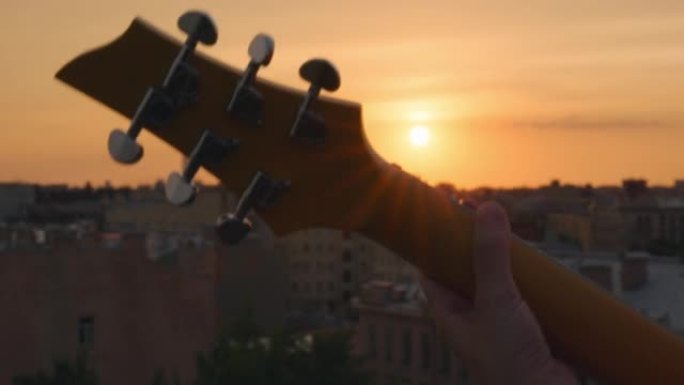 夏季屋顶音乐会上，剪影头颈吉他颈部在五颜六色的日落