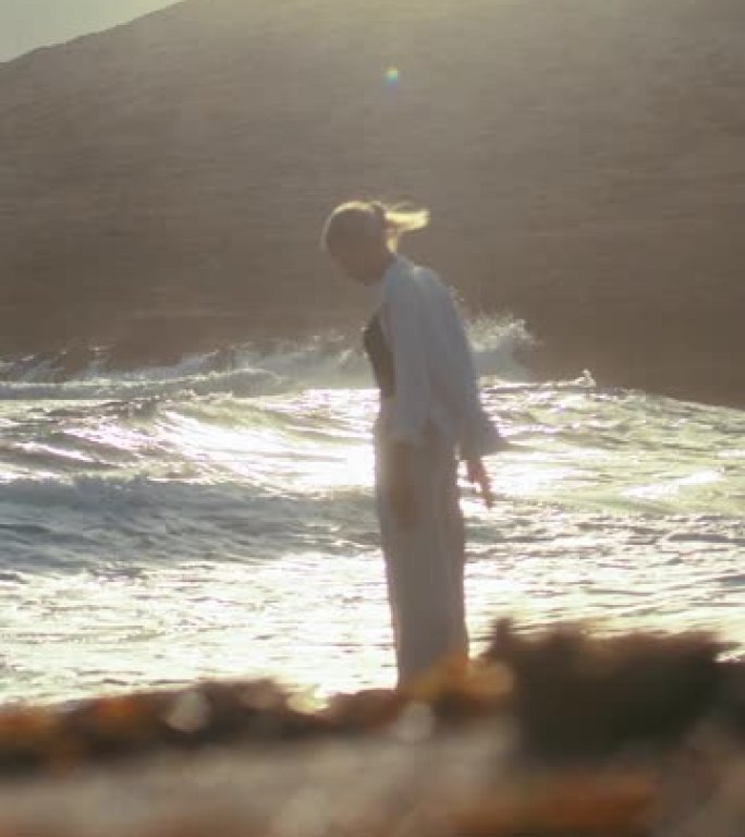 独自站在海滩上的女人。当海浪冲向她的脚下时，俯视遥远的大海垂直视频