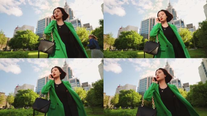 富有的亚洲女士在豪华城区散步，用新手机打电话，户外肖像