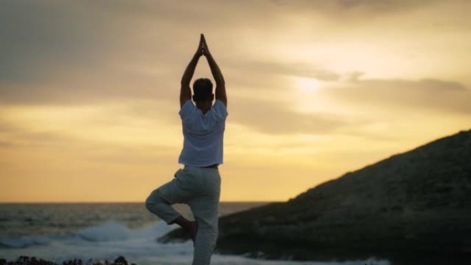 祈祷姿势的男人在海滩做瑜伽。山上美丽的日落