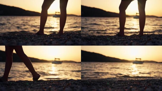 在金色的天空下日落时，用帆船在圆石滩上行走的特写女性腿
