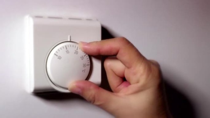 通过使用室内恒温器降低热量来节约能源。女性手。