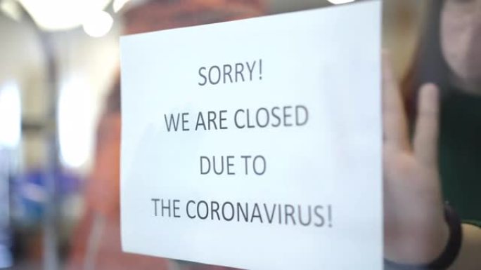 橱窗公告特写。模糊的高加索年轻店员附上通知抱歉，由于冠状病毒，我们关门了。由于新型冠状病毒肺炎大流行