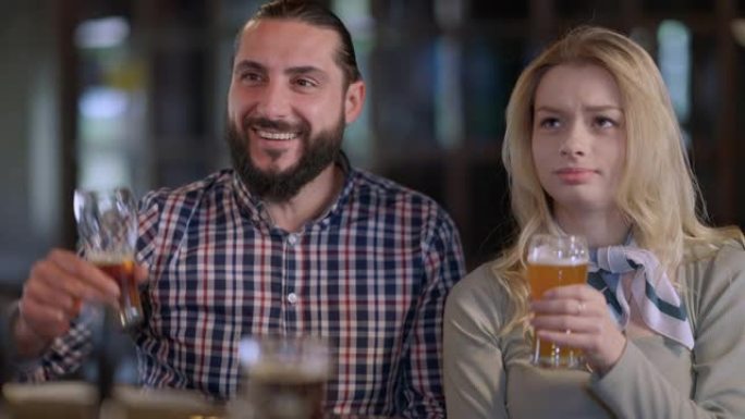 快乐微笑的男人在酒吧看足球比赛，和女人一起敬酒，欢呼胜利。正面胡须的高加索男朋友和美丽的女友在酒吧休