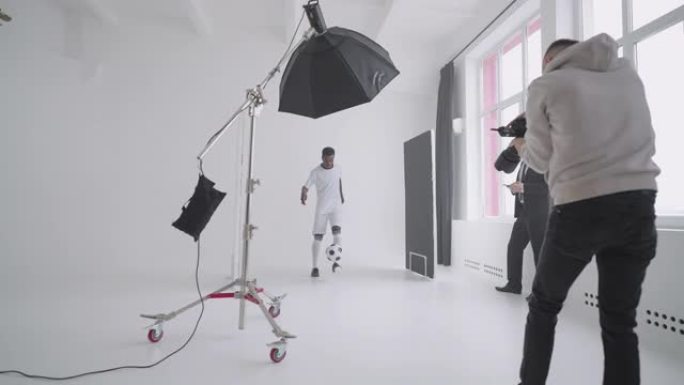 一名非洲裔美国足球运动员在摄影棚里对着摄影师的相机摆姿势，展示踢球技巧