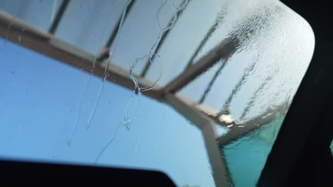 背景为蓝色晴空的高压清洗机清洁挡风玻璃。在户外晴天从洗水车车内拍摄。