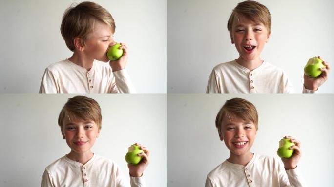 可爱的孩子男孩咬了一个绿色的苹果，咀嚼着，在白色背景下对着镜头微笑。健康的生活方式和饮食习惯。