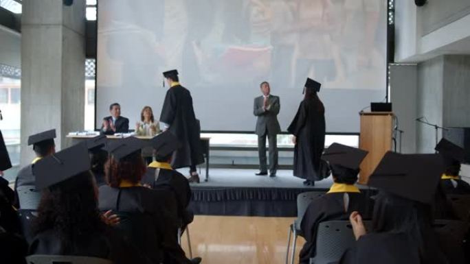 毕业生在与董事会成员和大学院长握手时获得文凭的后视图