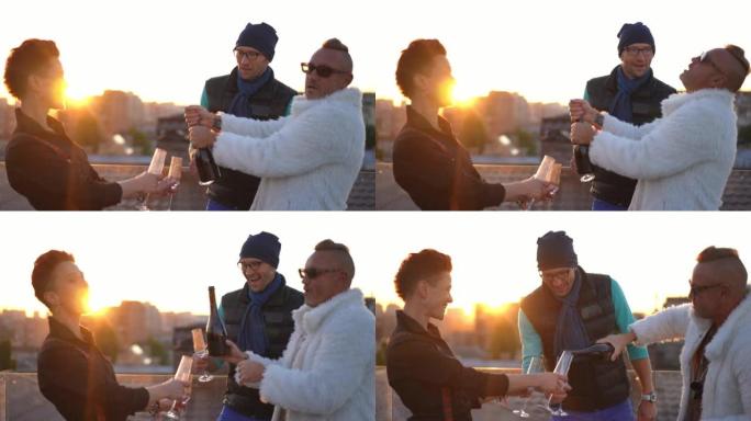 快乐的高加索成年朋友在城市屋顶的金色日落时打开香槟。快乐的男人和女人在周末在城市的屋顶上休息喝酒很开
