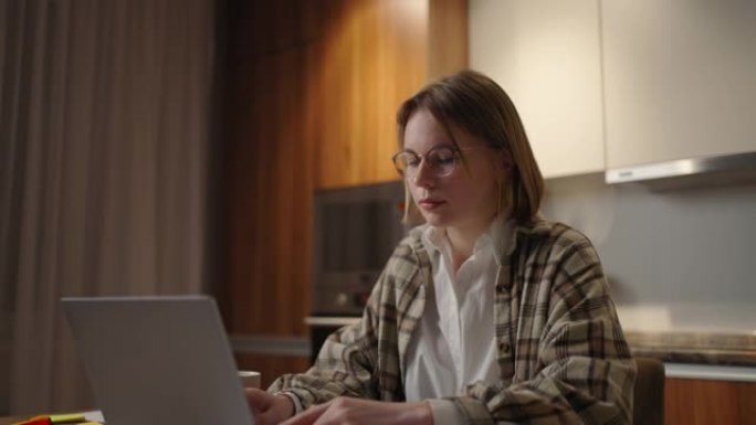 成熟的女商人在家工作，专注的女人正坐在家里的厨房里用笔记本电脑和纸质文件工作。笔记本电脑应用程序计算