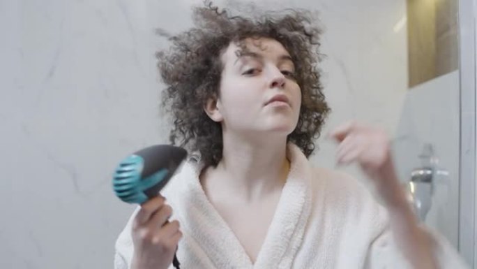 酒店浴室用吹风机给头发定型头发的卷发女人，美容程序