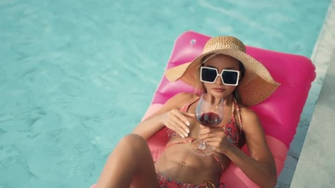 性感的女人和红色的葡萄酒在游泳池里放松。