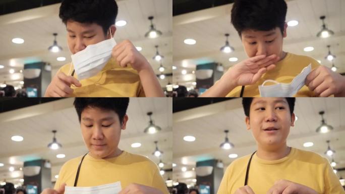 亚洲男孩在美食广场吃午饭前摘下口罩，这是新的正常生活方式概念。