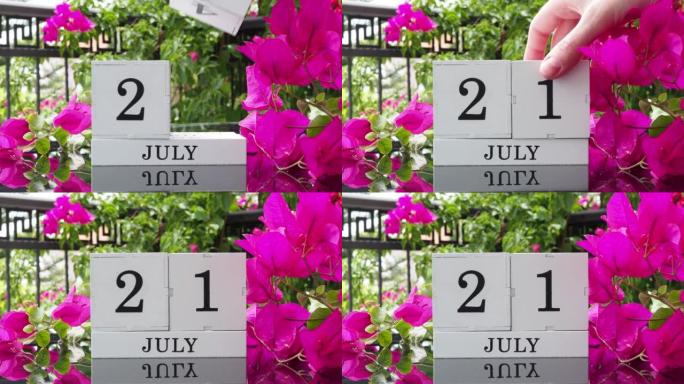 一个木制日历，有一个重要的活动，7月21日在一张有芙蓉花的桌子上，女人的手在日历上设定了日期。将日历
