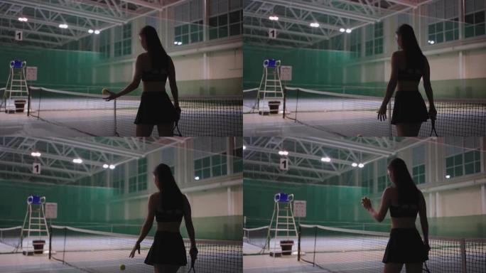 穿着运动服的运动女人正走在网球场上，拿着网球拍和投掷球，苗条的女性身材的后视