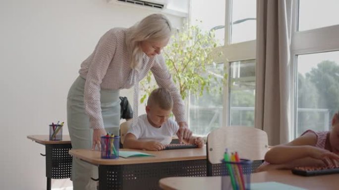 在小学课堂上: 热情的老师走在一排排聪明多样的孩子之间，讲解课程。一群聪明的多民族孩子学习新东西。侧