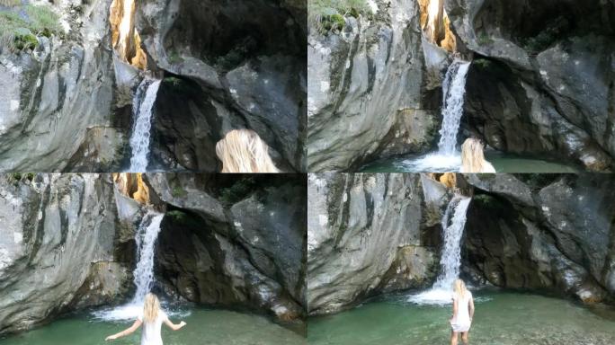 年轻女子涉水进入瀑布池，伸展手臂