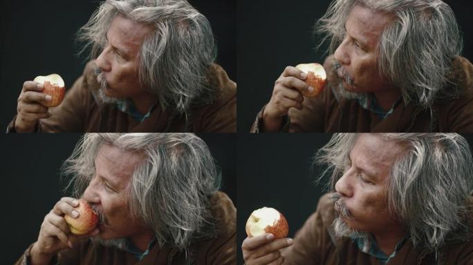 在黑色背景上吃苹果的老人