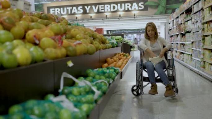 坐在轮椅上的成熟开朗的女人从零售陈列中挑选甜芒果，并把它们放入手提袋中