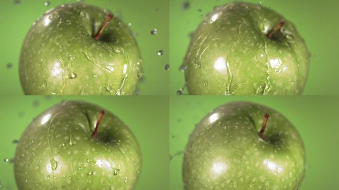 超级慢动作水滴在旋转的青苹果上。在绿色背景上。