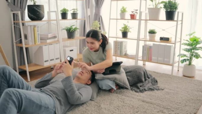 年轻夫妇在家里客厅内的在线平台上的智能手机商店观看应用程序。