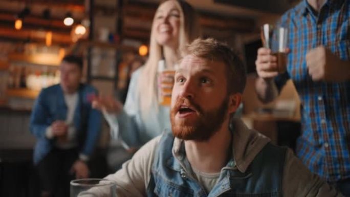 一个留着胡子的男性红发球迷和朋友在酒吧看足球的肖像。世界杯，足球，曲棍球，篮球，体育比赛。