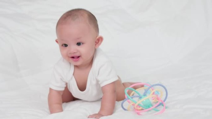 幸福的家庭，可爱的亚洲新生婴儿。在白色床上玩耍和爬行时，看着相机，笑容满面。天真的小新婴儿可爱。父母