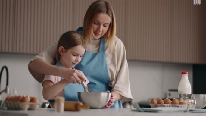 母亲正在教她的小女儿做饭，帮助鞭打奶油做蛋糕，妈妈和孩子的女孩