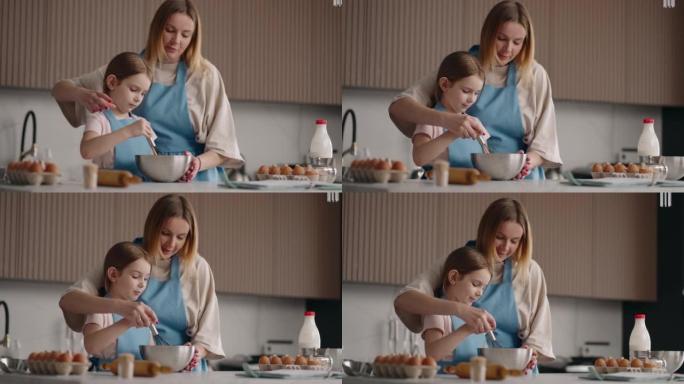 母亲正在教她的小女儿做饭，帮助鞭打奶油做蛋糕，妈妈和孩子的女孩