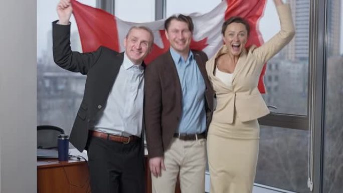 一群快乐快乐的商人在办公室里摆着加拿大国旗。快乐的男人和女人拿着国家象征欢欣鼓舞在室内创业成功。骄傲