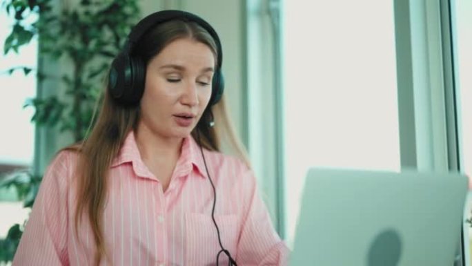 年轻迷人的女商人戴着耳机坐在办公室里使用电脑