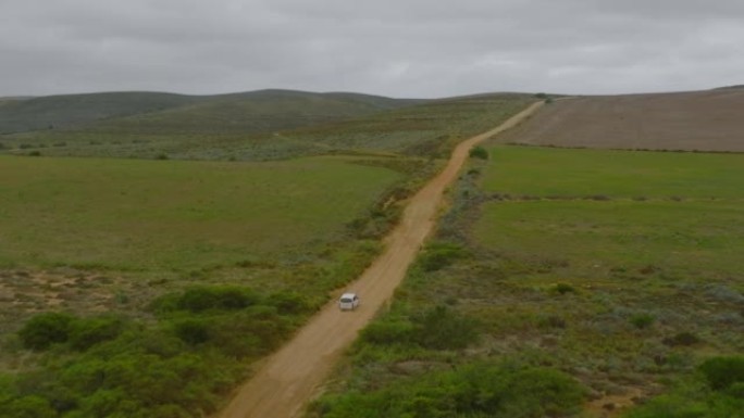 在景观中行驶的大型乘用车的前瞻性跟踪。通往绿色植被农田之间的土路。南非