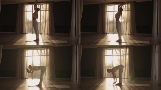 镜头耀斑: 一位穿着白色运动服的年轻女子在一个大大厅里伸展，大厅里有大窗户，采用慢动作方案，阳光透过