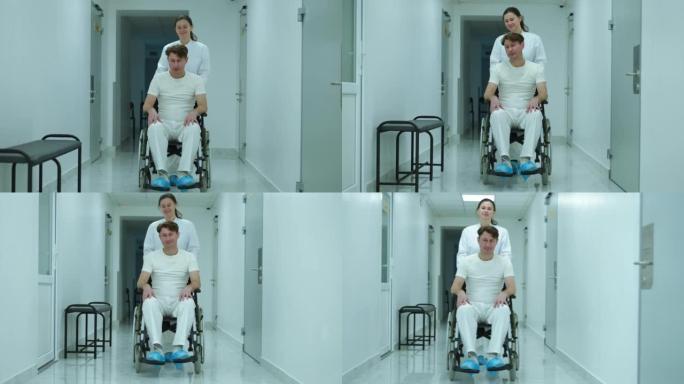 宽镜头肖像积极的医生说话的病人推着轮椅在医院的走廊。前视图白种人护士支持瘫痪病人滚动移动辅助装置在诊