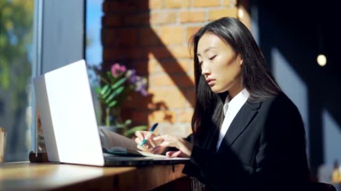 年轻的女性自由职业者或在网上工作或在咖啡馆远程学习的学生。穿着西装的亚洲女商人在工作场所的办公热办公