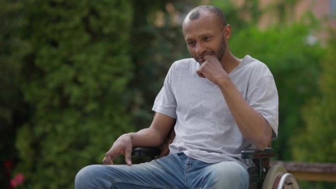 坐在户外轮椅上的体贴的非洲裔美国人的中等镜头肖像。成年悲伤的残疾人想在后院的夏日花园里移开目光。生活