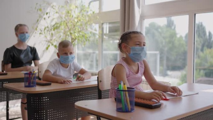 举手回答老师的问题。新型冠状病毒肺炎大流行期间在学校戴口罩的多种族儿童。
