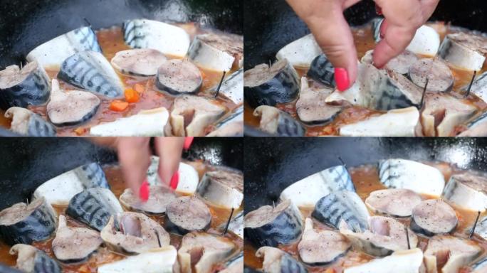 一个女人把鲭鱼放在装有蔬菜的铸铁大锅中。在户外准备食物。特写