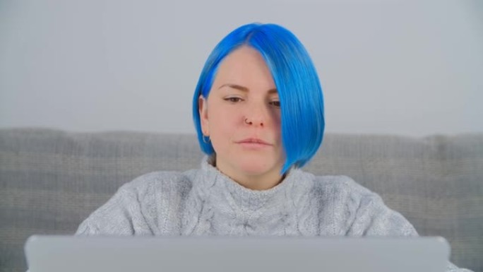 千禧一代白人妇女的肖像，鲍勃发型和染成蓝色的头发在家里的笔记本电脑上工作