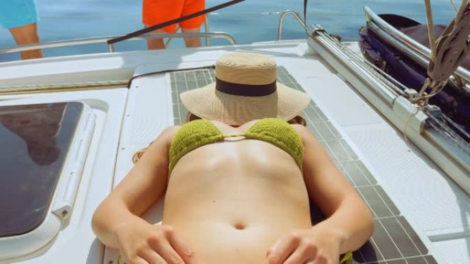 年轻女子在游艇上晒日光浴，脸上戴着软呢帽