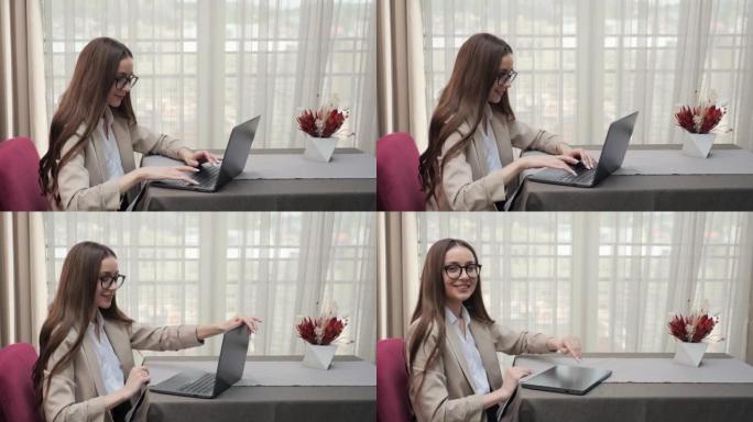 微笑的女人在酒店休息室的笔记本电脑上打字。女商人完成关闭笔记本电脑的工作，并在餐厅大堂看着相机。快乐