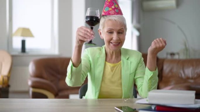 自信的女人在慢动作中敬酒喝红酒的肖像。穿着派对帽子的美丽白人女商人从家庭办公室在线庆祝假期。远程工作