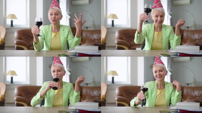 自信的女人在慢动作中敬酒喝红酒的肖像。穿着派对帽子的美丽白人女商人从家庭办公室在线庆祝假期。远程工作