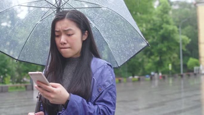 年轻的亚洲妇女收到分手信息，站在雨伞下的雨中