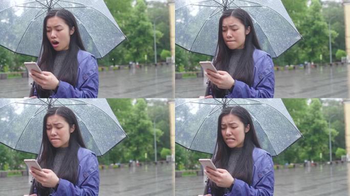 年轻的亚洲妇女收到分手信息，站在雨伞下的雨中